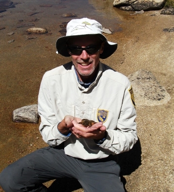 Jim smiling and holding a frog beside a lake