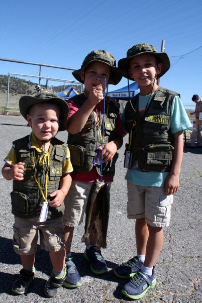 three children smiling, holding up rainbow trout