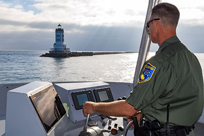 wildlife officer piloting a boat with lighthouse in background 
