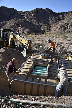 Four men place a 2,300-gallon plastic tank into a rectangular hole in the southern California desert.