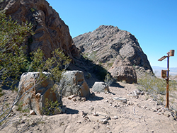 Two fake rocks and a small solar panel on a post, near real rocky terrain in the southern California desert