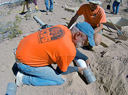 Two men in orange T-shirts place water pipes into a trench in the desert