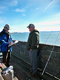 Two men on a pier, one with a clipboard and the other with a fishing pole