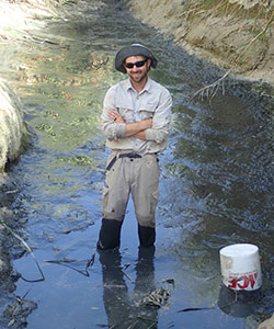 scientist, nick buckman smiling, standing in a streams with his arms crossed