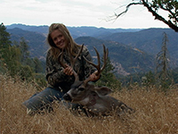 A female hunter poses in dry grass with the deer she killed