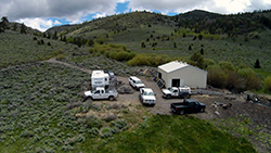 A small building, trailer, and five trucks on an isolated hill