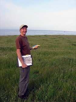 A man stands in coastal grassland with the ocean in background