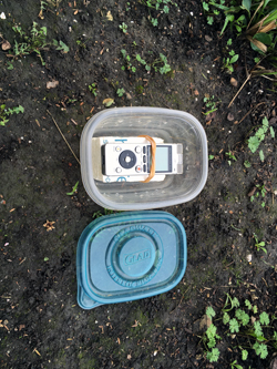 An audio recording device in a semi-clear, plastic container on dark brown ground