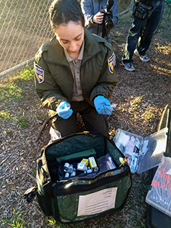 woman in fish and wildlife uniform selects small instruments from backpack