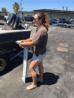 Woman standing in parking lot next to outboard motor boat on trailer