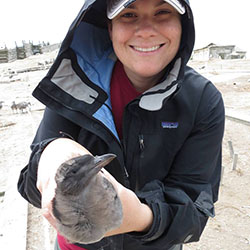 Woman wearing windbreaker jacket with hood over hat and head while holding marine bird