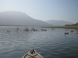Bow of kayak floating on calm lake with foggy mountains in background