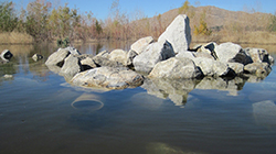 Lake with partially submerged pile of rocks with trees and mountain in the background
