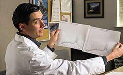 Man wearing white lab coat holding up two sheets of white paper with graphs.