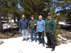 Four men standing next to each other with snow on the ground and trees in the background