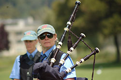 Woman in blue shirt and black vest with green ball cap holding bagpipes.