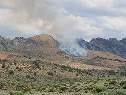Smoke from a smoldering fire in a dry field with mountains and clouds in the sky