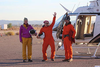 The desert bighorn crew smiles and poses for the camera in front of the helicopter they have used to survey sheep. They are wearing heavy, bright orange jumpsuits - link open in new window.